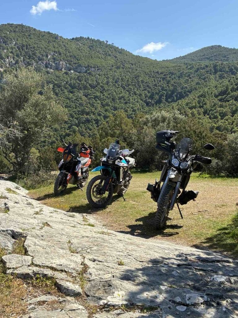 Τρεις adventure μοτοσυκλέτες (CFMOTO 450MT, KTM 790, Voge 300 Rally) σε στάση στα Γεράνεια Όρη, με πράσινες πλαγιές στο φόντο